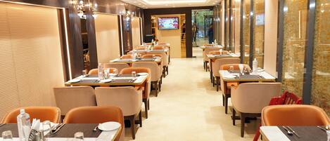 A restaurant with multiple tables and chairs, a television screen, and a tiled floor.