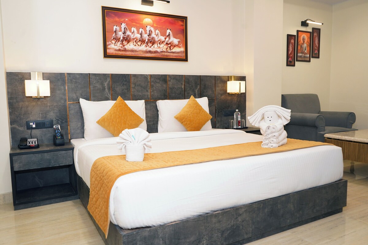 Una habitación de hotel con una cama grande, dos mesitas de noche, una silla y un cuadro en la pared.