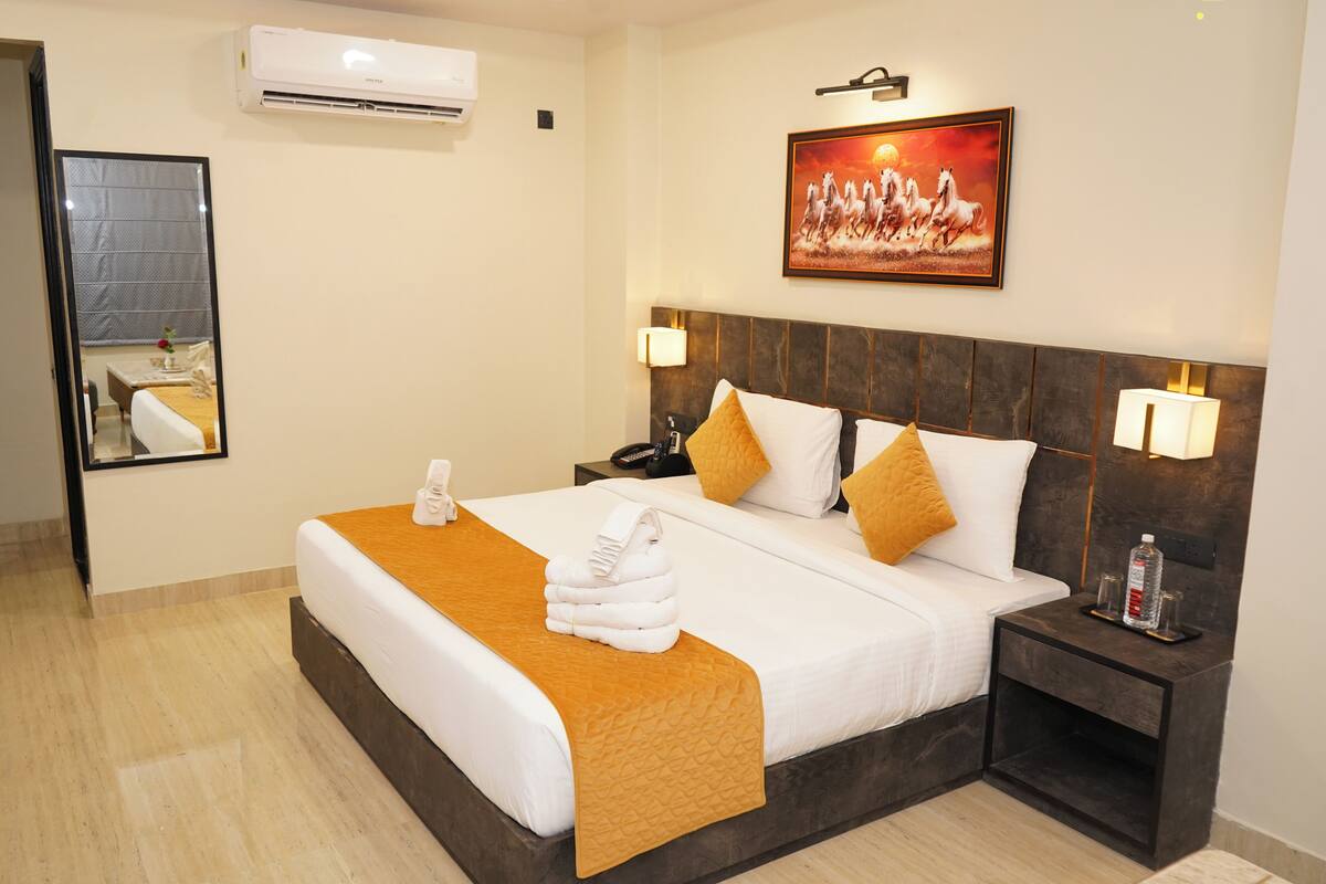 A hotel room with a bed, a nightstand, a mirror, an air conditioner, and a painting on the wall.