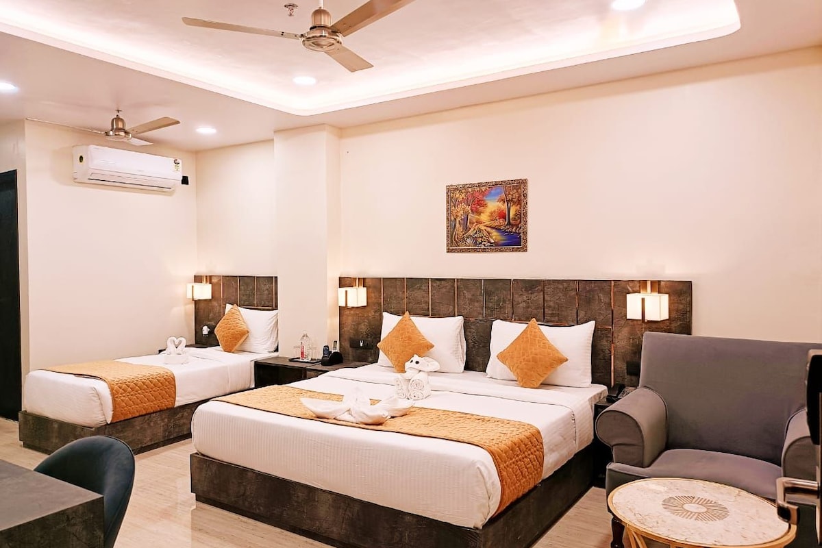 A hotel room with two beds, a sofa, a small table, and a ceiling fan.