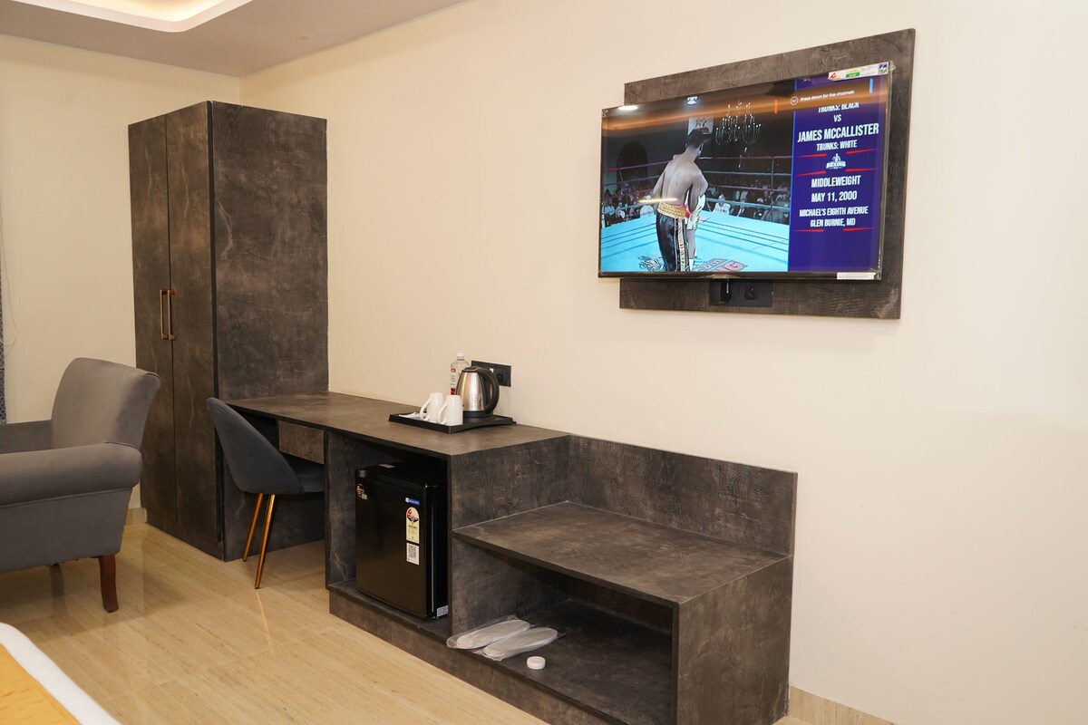 A modern living room with a dark wood cabinet, a small black refrigerator, a gray sofa, and a flat-screen TV mounted on the wall displaying a boxing match.