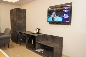 Una sala de estar moderna con un mueble de madera oscura, un refrigerador negro pequeño, un sofá gris y un televisor de pantalla plana montado en la pared mostrando un combate de boxeo.