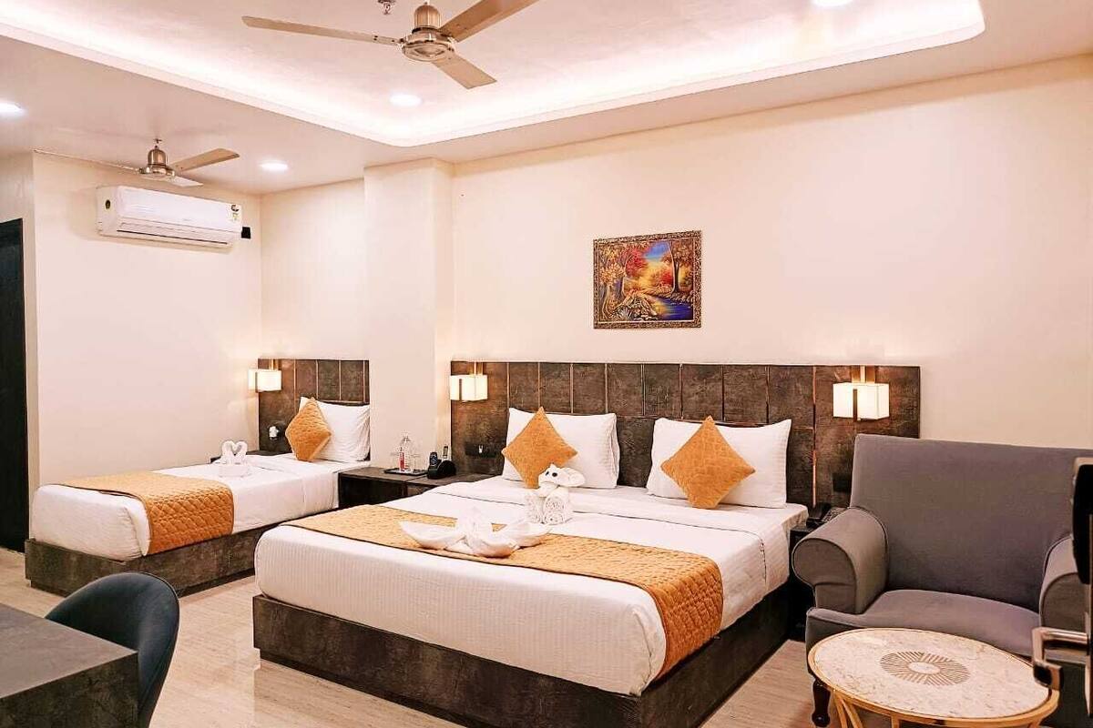 A hotel room with two beds, a sofa, a small table, and a ceiling fan.