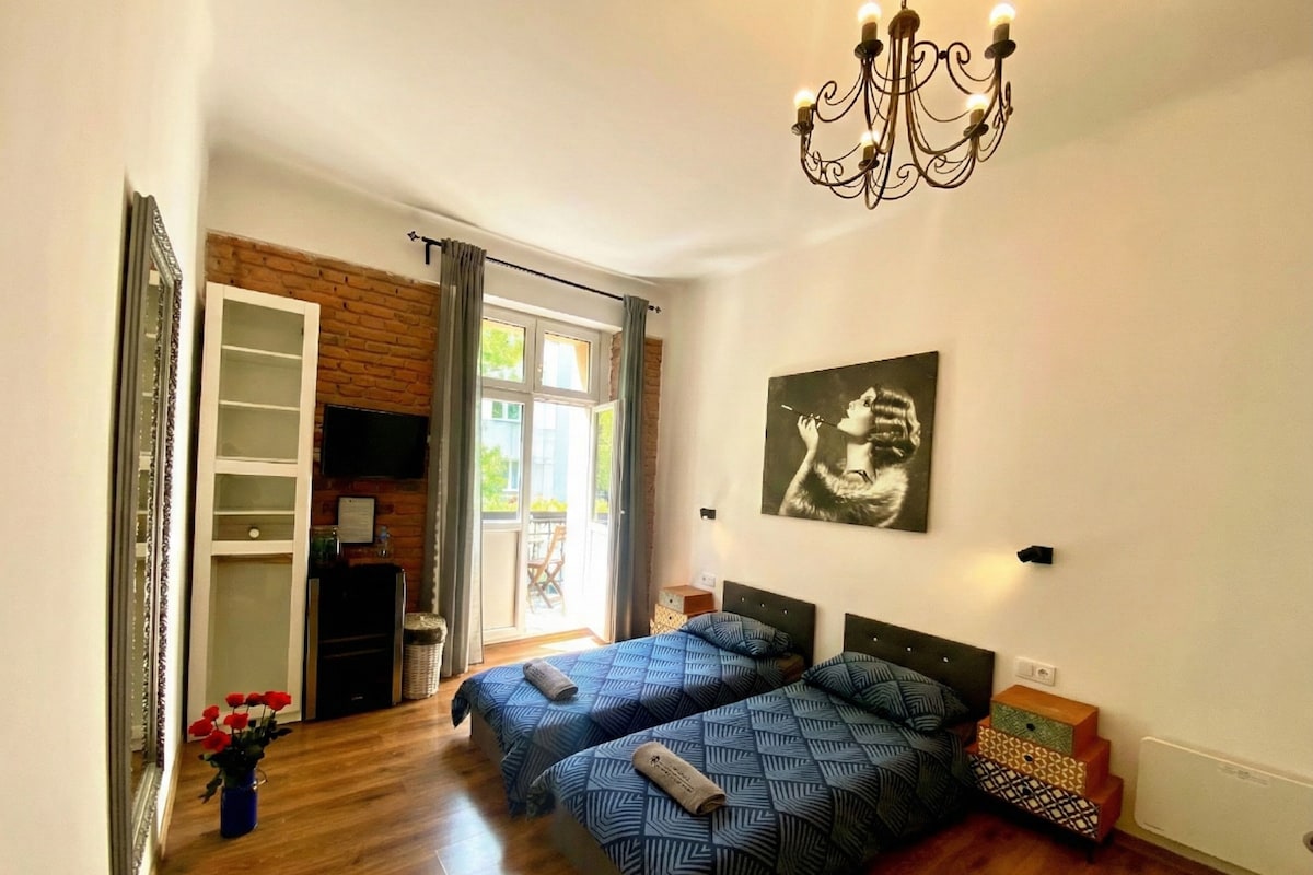 Een slaapkamer met twee bedden, een kroonluchter, een schilderij en uitzicht op het groen.
