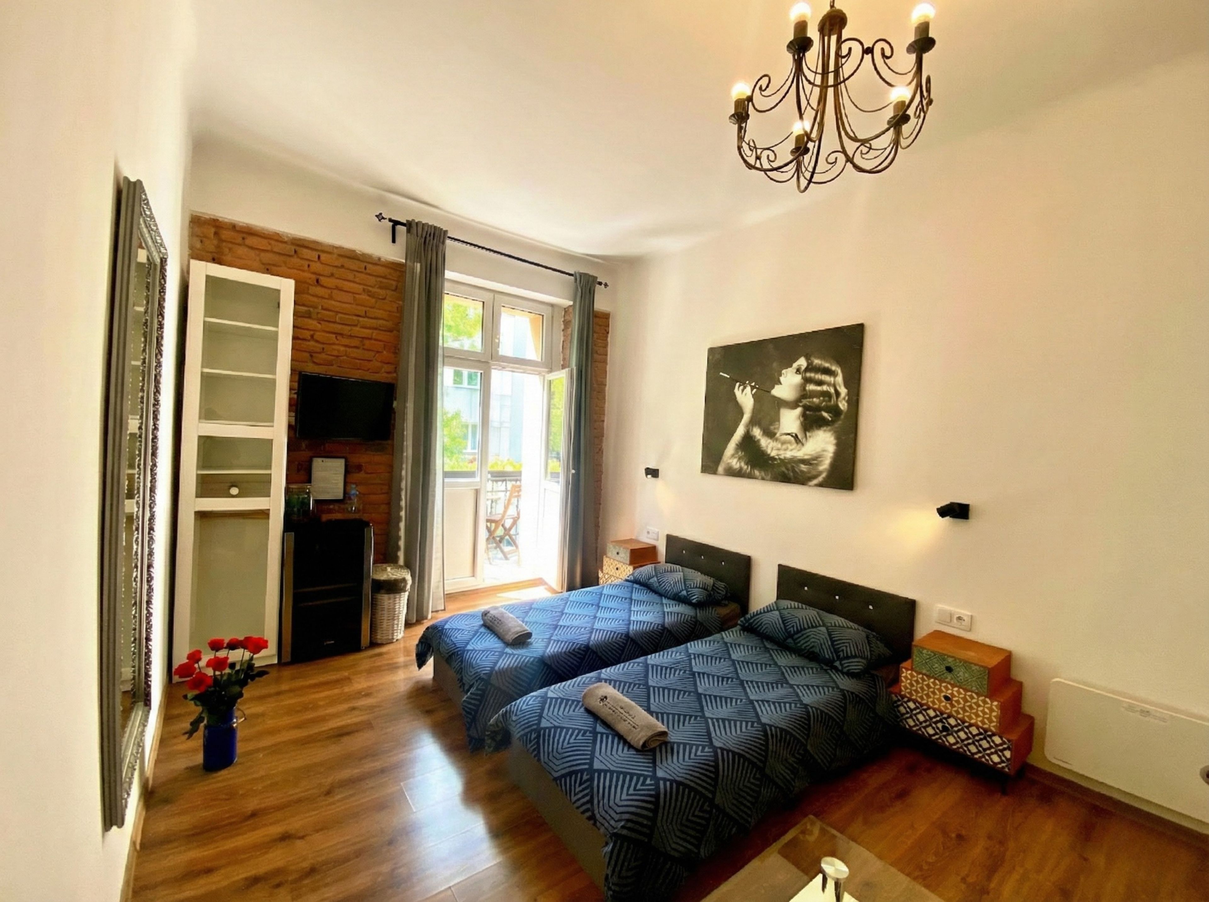 Een slaapkamer met twee bedden, een kroonluchter, een schilderij en uitzicht op het groen.