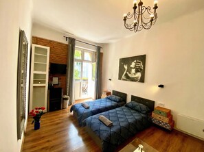 Ein Schlafzimmer mit zwei Betten, einer Kristallleuchtre, einem Gemälde und Blick ins Freie.
