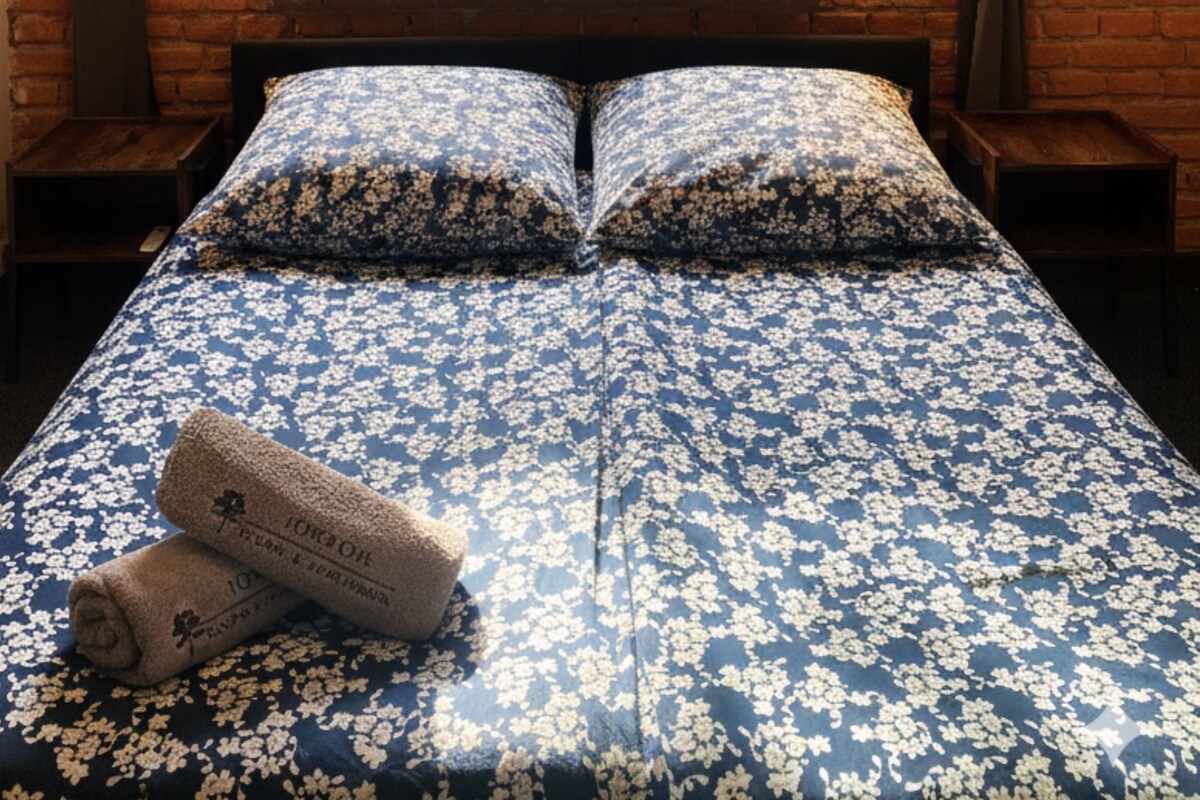 Ein Bett mit einer blumigen Tagesdecke, zwei Kissen und einem zusammengerollten Handtuch.