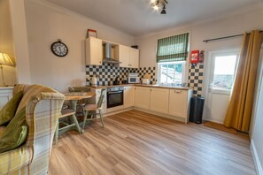 A compact kitchen with a dining area, featuring a checkered backsplash, a clock, and a fire extinguisher. - Host Stay Sea View Cottage (Scarborough)