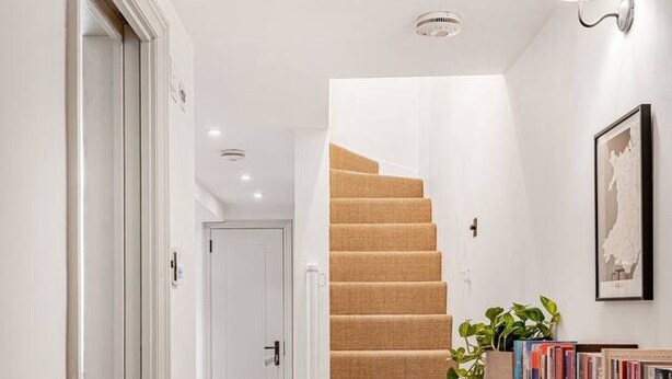 A staircase with a wooden finish, a white door at the top, and a shelf with books and a plant. - Notting Hill 4-bed Private Garden Home Office (London)