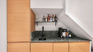 A kitchen with a built-in sink, a marble countertop, wooden cabinets, and a shelf with various bottles. - Notting Hill 4-bed Private Garden Home Office (London)