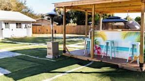 Un patio trasero con césped artificial, una zona de barbacoa y una pérgola de madera.