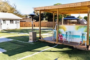 Ein Garten mit künstlichem Rasen, Grillplatz und einer Holzpergola.