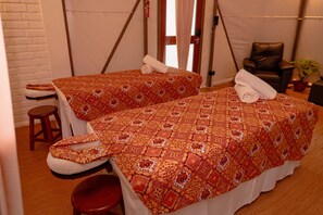 Two single beds with patterned bedding, a wooden stool, and a massage chair in a room with white walls and a brick accent wall. - The Anmon Resort Bintan (Bintan)