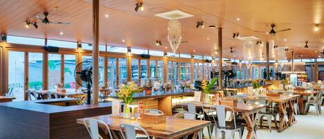 A spacious restaurant with high ceilings, wooden beams, and large windows offering views of the city.