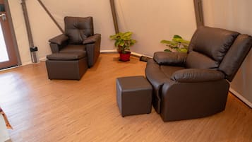 A tented room with two brown leather sofas and a matching ottoman, a red potted plant, and a wooden floor.