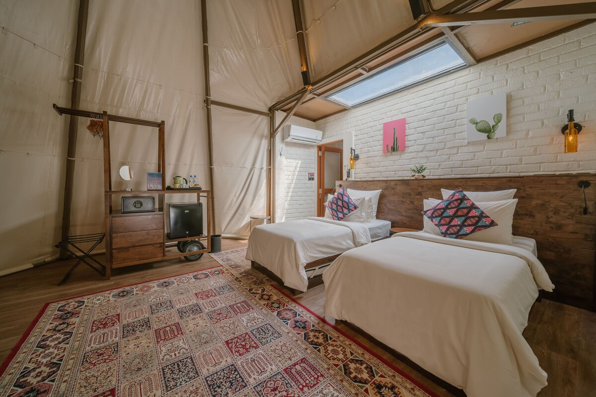 A tented room with two beds, a patterned rug, and a brick wall with artwork.