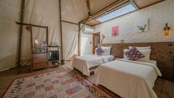 A tented room with two beds, a patterned rug, and a brick wall with artwork.