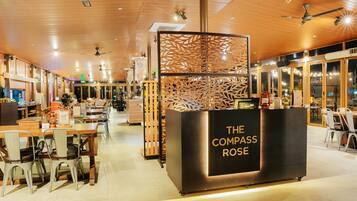 L’intérieur d’un restaurant présente un plafond en bois, des tables, des chaises et un comptoir d’accueil portant l’inscription « The Compass Rose ».