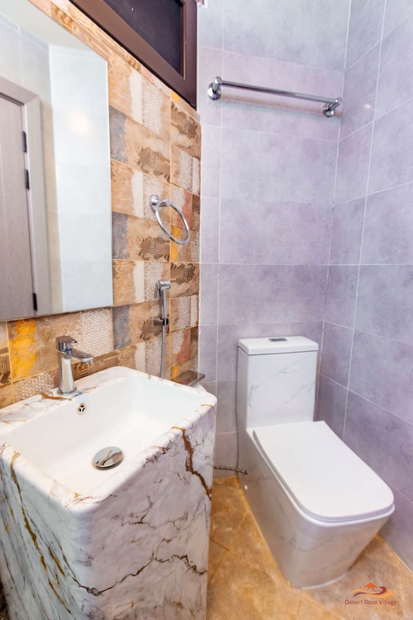 A bathroom with a marble sink, a toilet, and a shower area. - Desert Rose Village (Abu Dhabi)