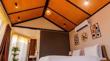 A hotel room with a wooden ceiling, a bed with white and red bedding, a patterned rug, and a potted plant.