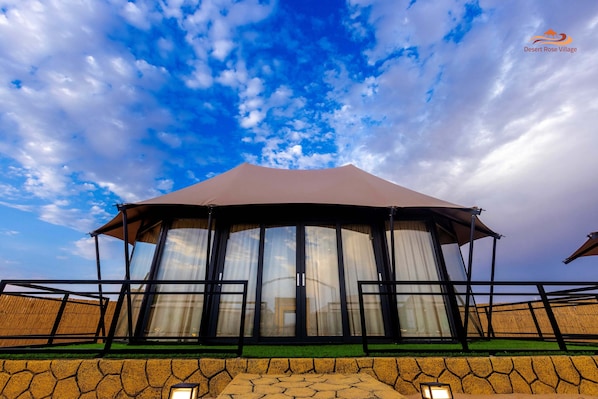 A large, covered pavilion with a curved roof and glass doors, set against a backdrop of a blue sky with clouds. - Desert Rose Village (Abu Dhabi)