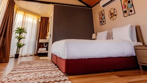 A hotel room with a wooden ceiling, a bed with white and red bedding, a patterned rug, and a potted plant. - Desert Rose Village (Abu Dhabi)