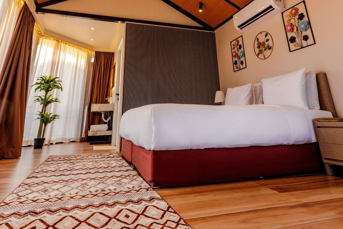Ein Hotelzimmer mit Holzboden, einem Bett mit weißer und roter Bettwäsche, einem gemusterten Teppich und einer Topfpflanze.