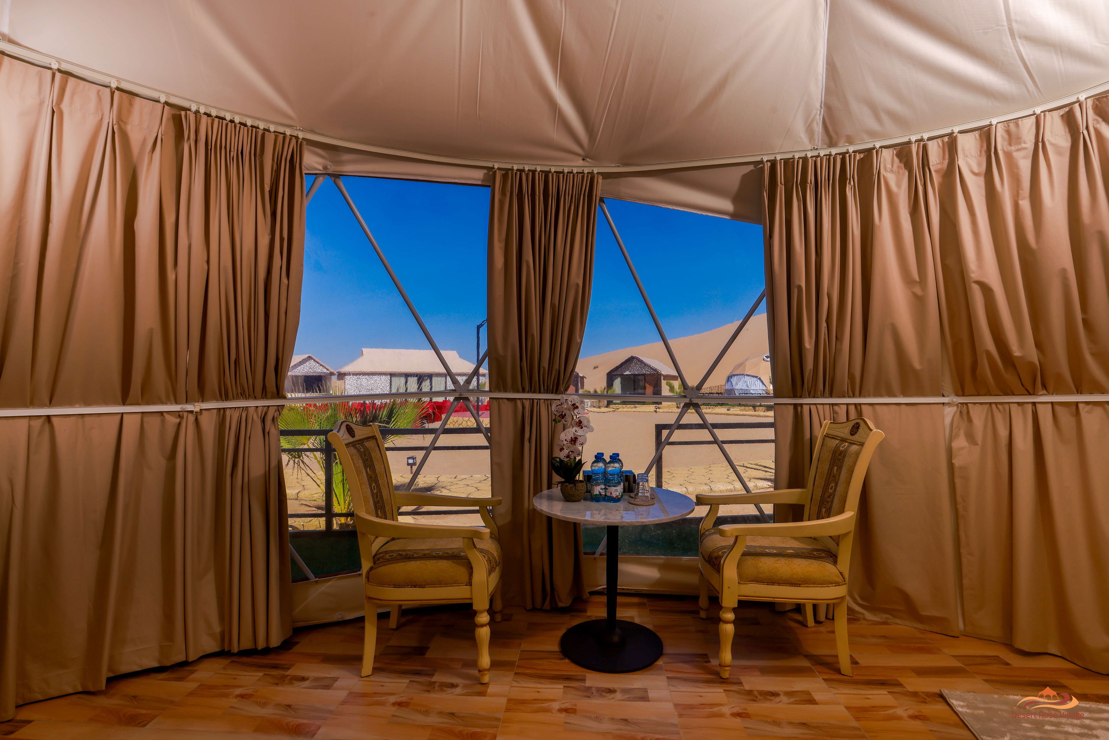A tented room with two chairs, a table, and a view of a desert landscape.