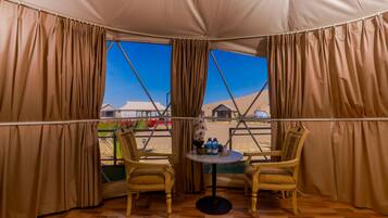 A tented room with two chairs, a table, and a view of a desert landscape.