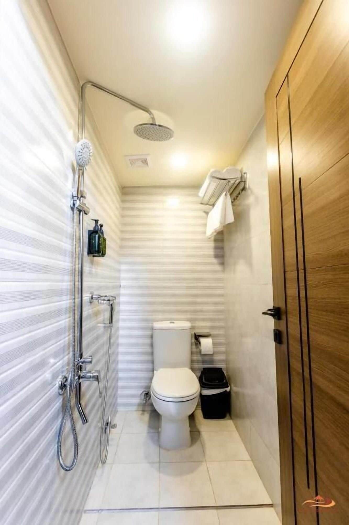 A compact bathroom with a shower, toilet, and a wooden wardrobe.