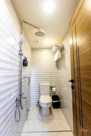 A compact bathroom with a shower, toilet, and a wooden wardrobe. - Desert Rose Village (Abu Dhabi)