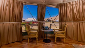 A tented room with two chairs, a table, and a view of a desert landscape. - Desert Rose Village (Abu Dhabi)