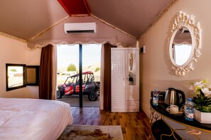 Un dormitorio con cama, tocador con espejo, escritorio con hervidor y vista a un vehículo rojo en el exterior.