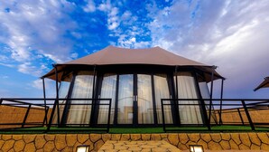 A large, covered pavilion with a curved roof and glass doors, set against a backdrop of a blue sky with clouds. - Desert Rose Village (Abu Dhabi)