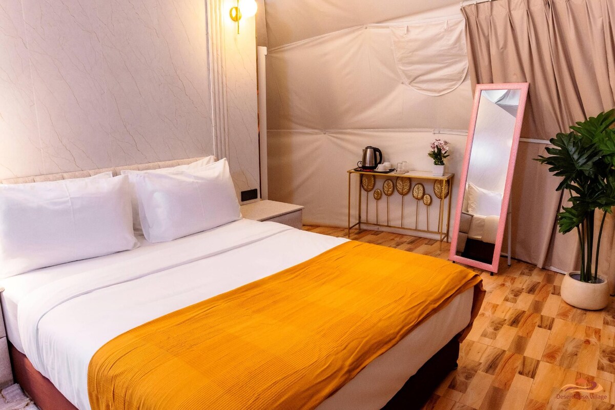 A hotel room with a bed, a bedside table, a mirror, a small table with a plant, and a curtain.
