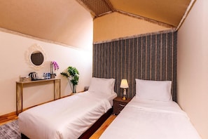 Habitación de hotel con dos camas, una mesita de noche con lámpara, un espejo y una planta pequeña.