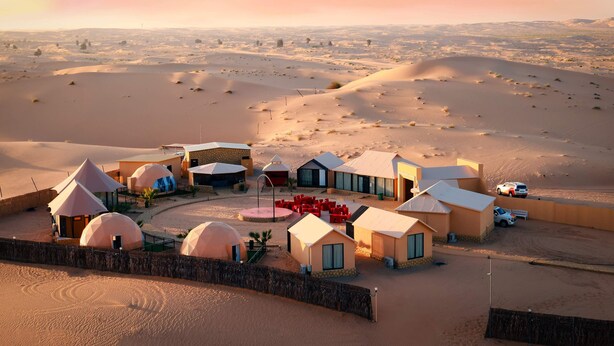 A desert resort with dome-shaped accommodations, a central courtyard with red chairs, and a fenced perimeter. - Desert Rose Village (Abu Dhabi)