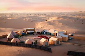 A desert resort with dome-shaped accommodations, a central courtyard with red chairs, and a fenced perimeter. - Desert Rose Village (Abu Dhabi)