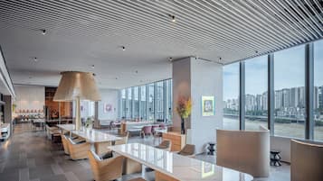 A modern hotel lobby with a large open space, seating areas, and a view of a cityscape through large windows.