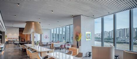 A modern hotel lobby with a large open space, seating areas, and a view of a cityscape through large windows.