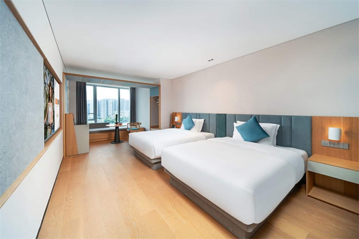 A hotel room with two beds, a desk, and a view of the city.