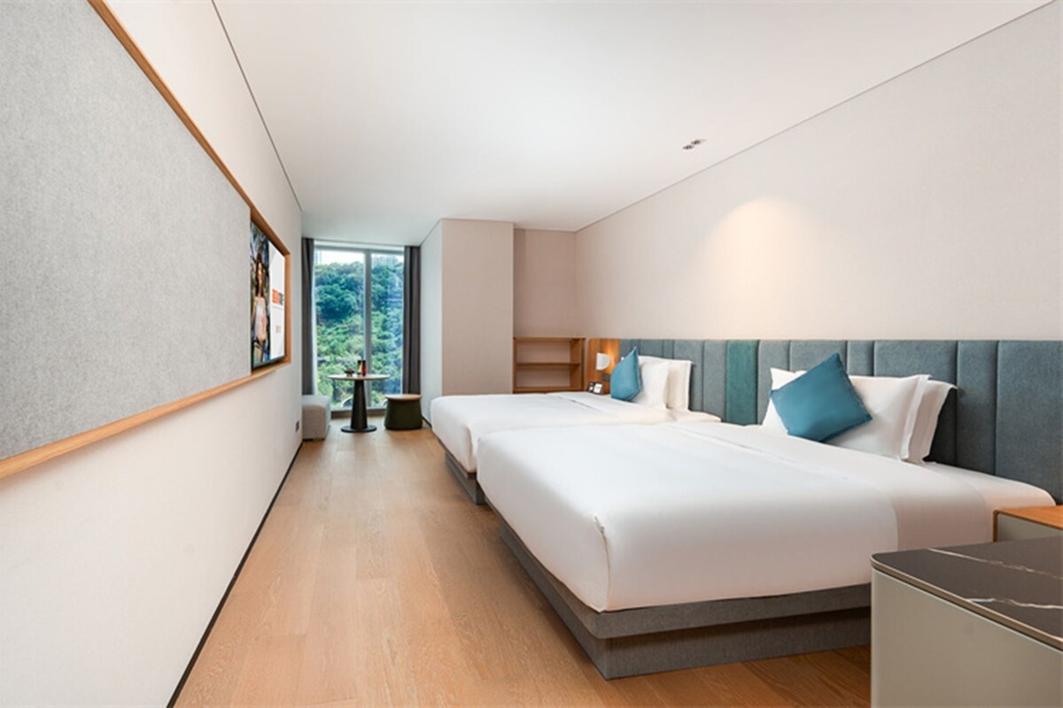 Une chambre d’hôtel moderne, dotée d’un grand lit, d’un bureau et offrant une vue sur la verdure environnante.