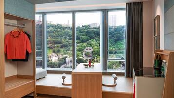 Una habitación de hotel moderna con un amplio ventanal que ofrece vistas a una ladera verde y exuberante. Hay un banco de madera con una mesita y elementos decorativos frente al ventanal.