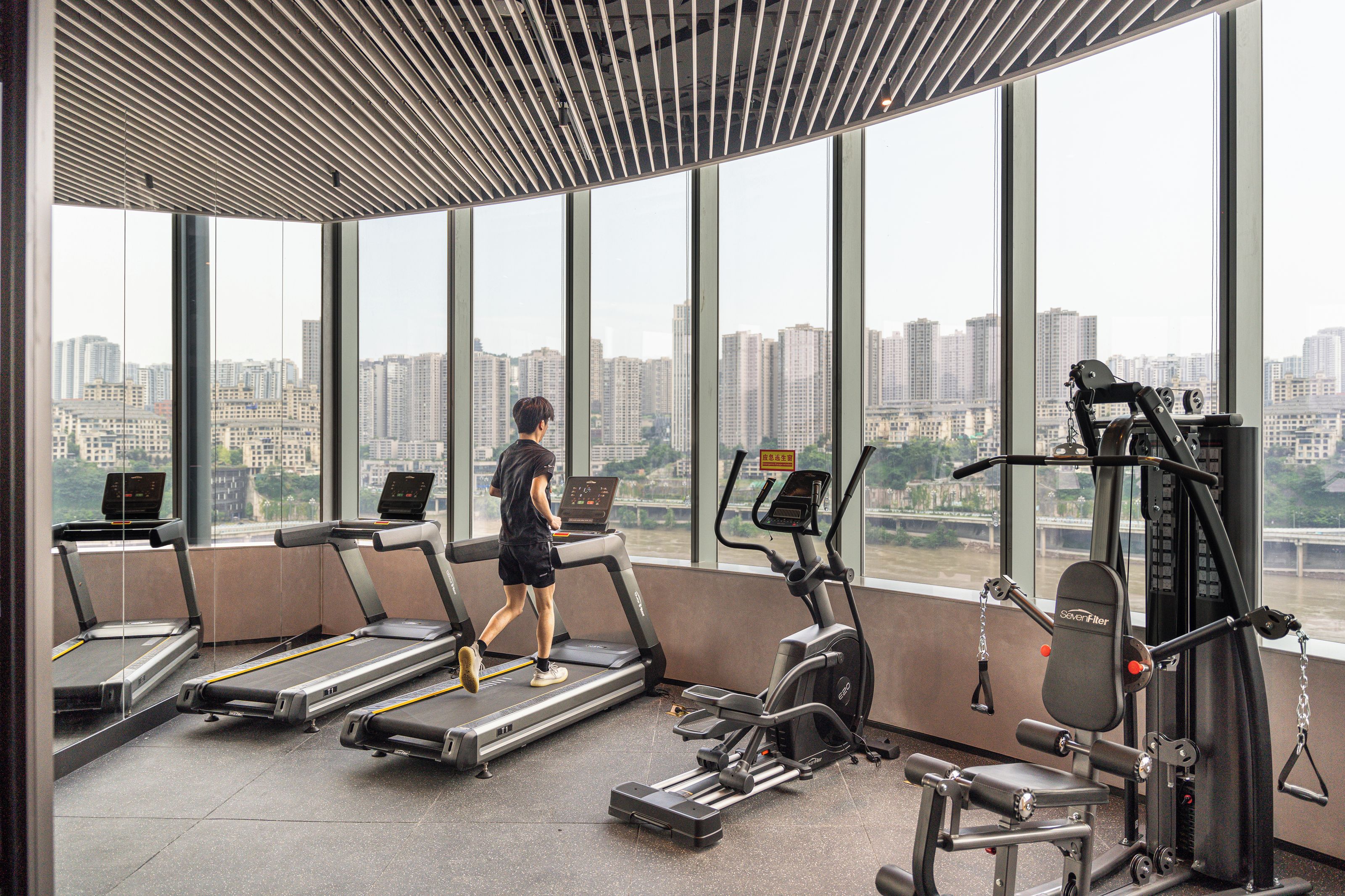 A gym with treadmills, a weight machine, and a large window overlooking a cityscape.