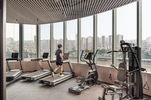 Une salle de sport équipée de tapis de course, d’une machine de musculation et d’une grande fenêtre donnant sur un paysage urbain.