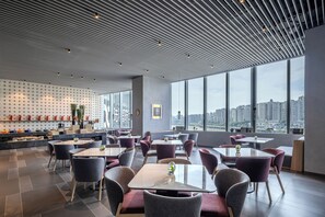 Un restaurant moderne offrant une vue sur la ville, avec un mur décoré de motifs, des tables et des chaises.