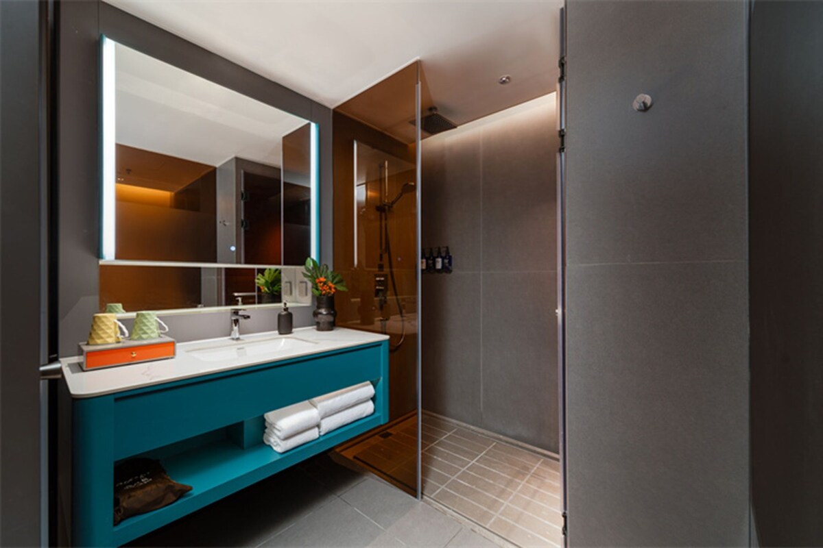 A modern bathroom with a large mirror, a blue vanity, and a walk-in shower.