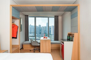 Camera d'albergo con un letto, una scrivania, una sedia, un armadio, una finestra con vista sulla città e un angolo cottura.