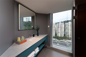 Une salle de bain moderne avec un grand miroir, un lavabo et une vue sur le paysage urbain, visible à travers une grande fenêtre.