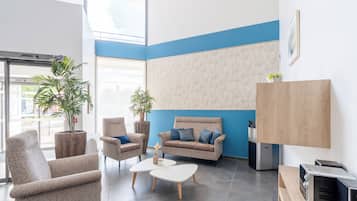 Un vestíbulo moderno con un sofá gris, sillones, una mesa de centro y una pequeña cocina.